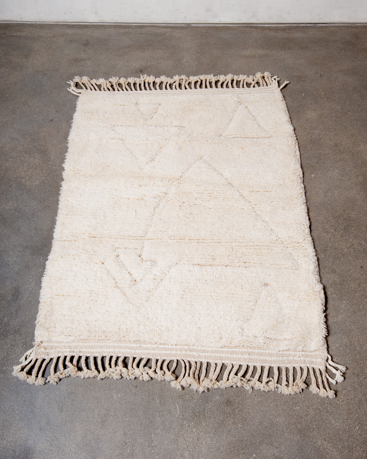 Beniourain rug in cream wool laying on concrete studio floor.